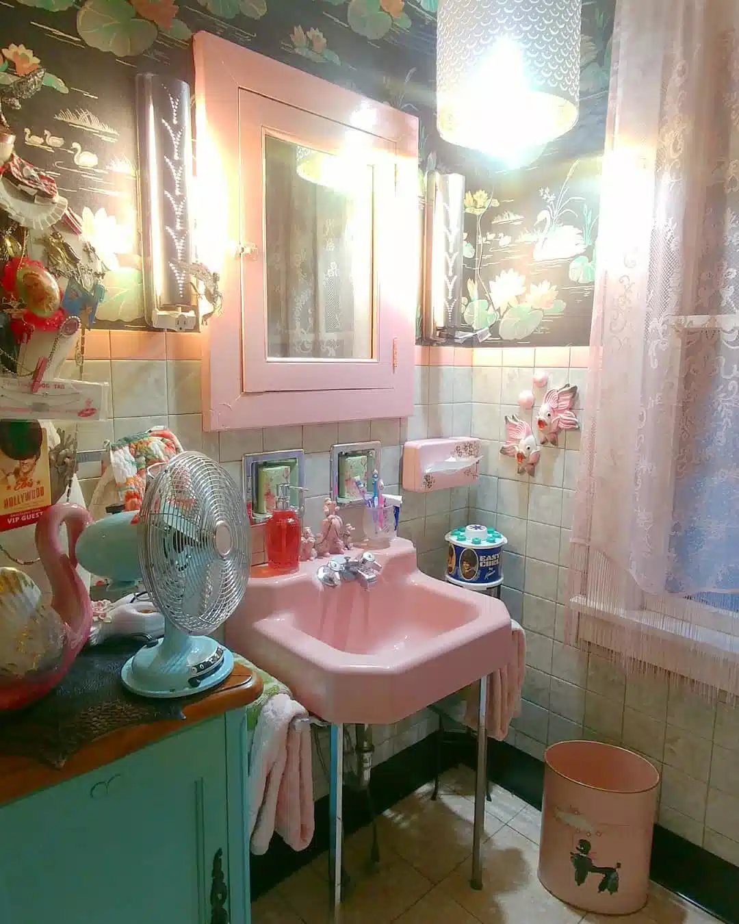 Retro bathroom with pink sink, pink mirror, aqua cabinet, vintage fan, and colorful accessories