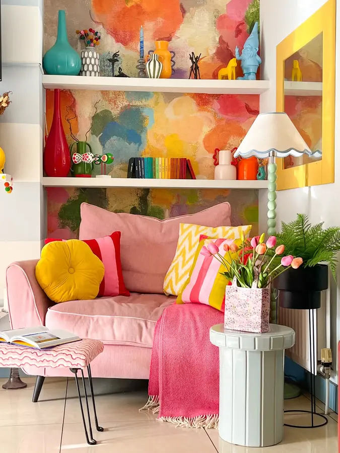 Colorful living room shelves with abstract multicolor backing, books, decor, plants, and a soft pink lounge chair