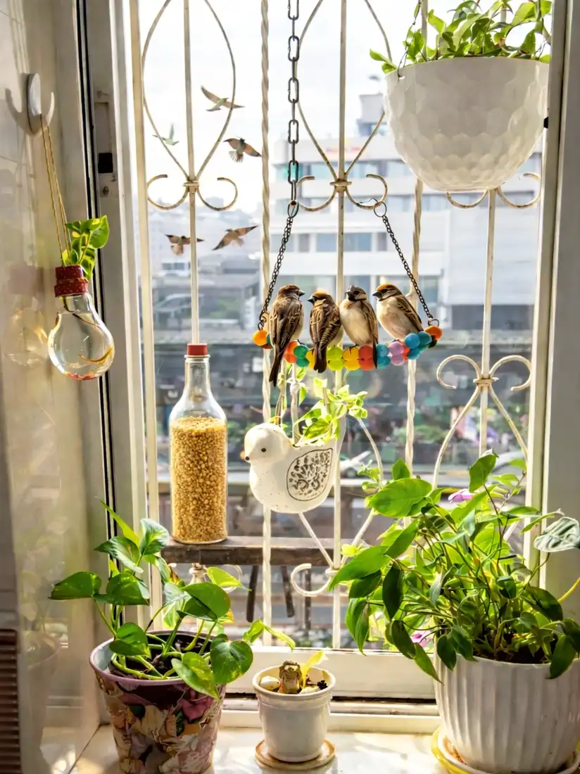 Kitchen window with leafy plants, hanging bird decorations, beads, and a white hanging planter