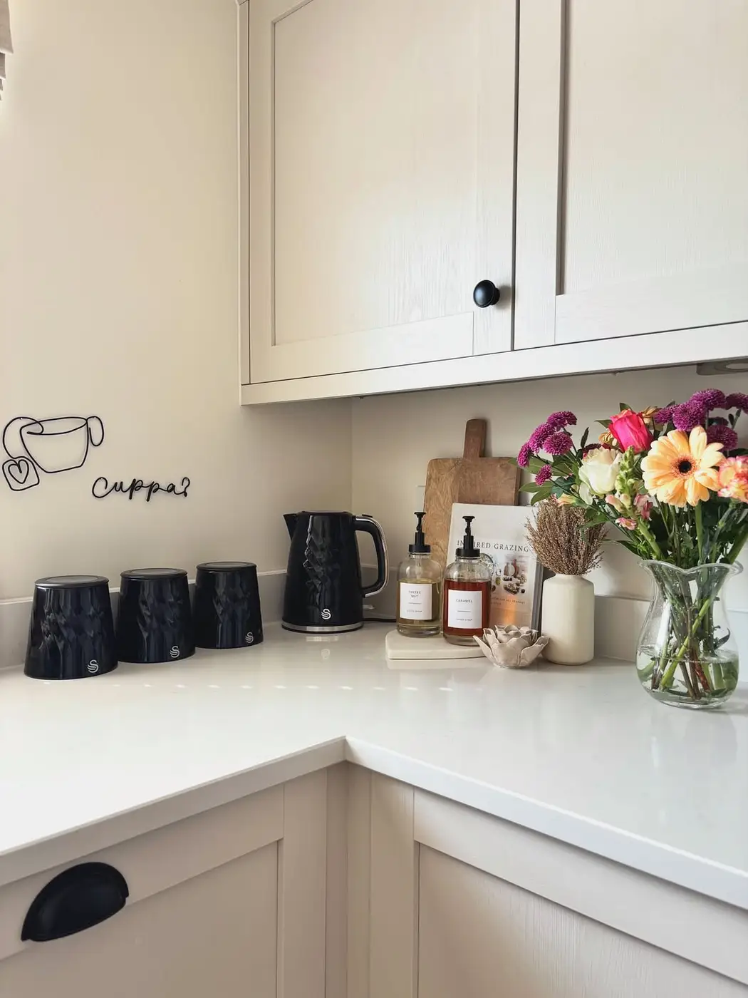 Bright white kitchen counter with black kettle, colorful flower bouquet, cutting board and soap bottles