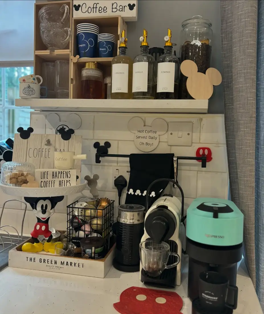 Mickey-inspired coffee bar with themed decor, syrup bottles, pod storage, mugs, and multiple coffee machines