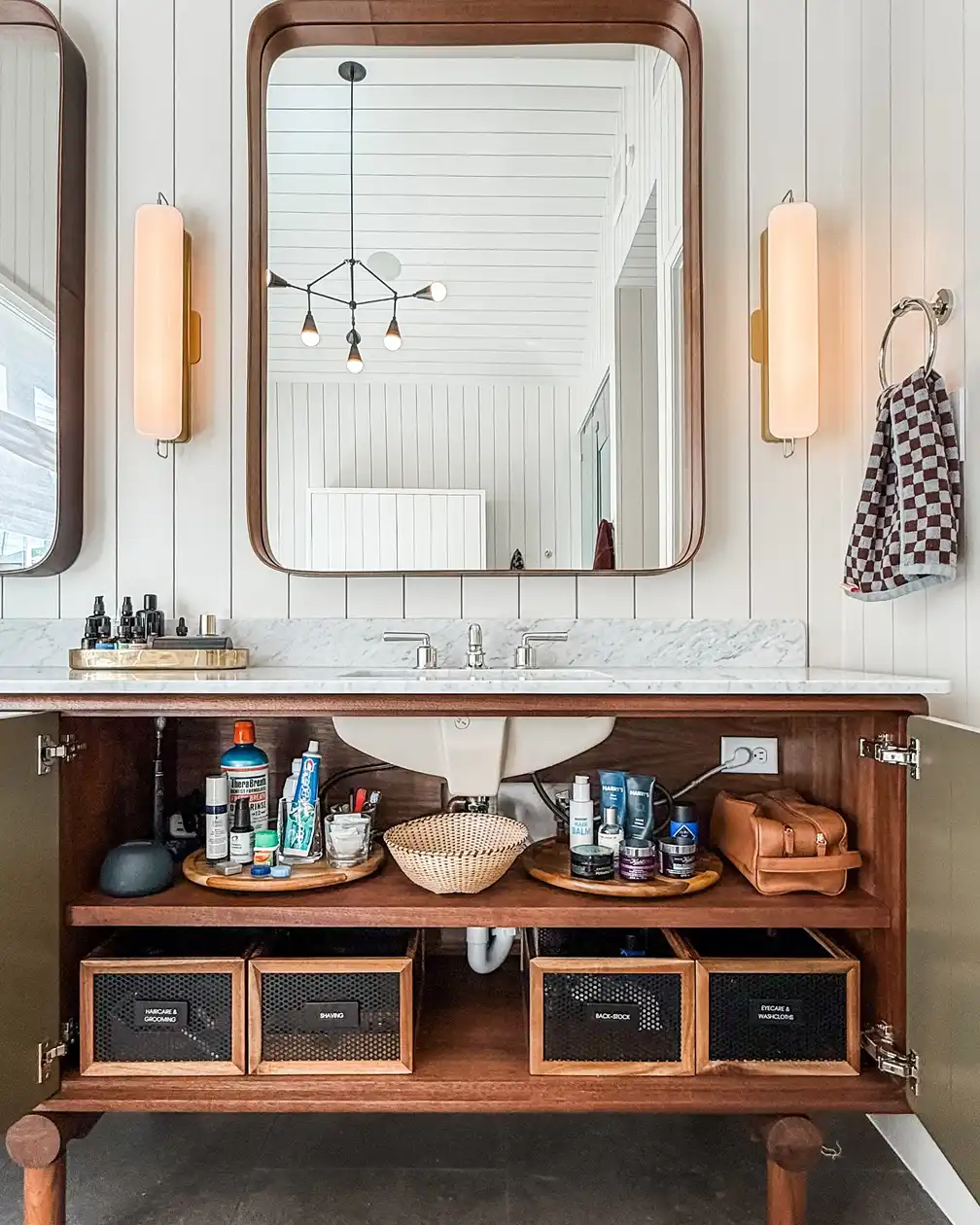 Bathroom vanity shelves with round toiletry trays, woven basket, bottles, and labeled wooden storage drawers