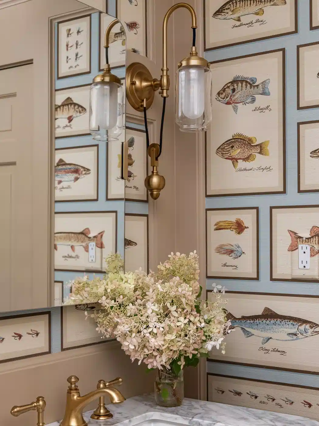 Bathroom with blue fish wallpaper, brass lighting, brass fixtures, marble counter, and round mirror