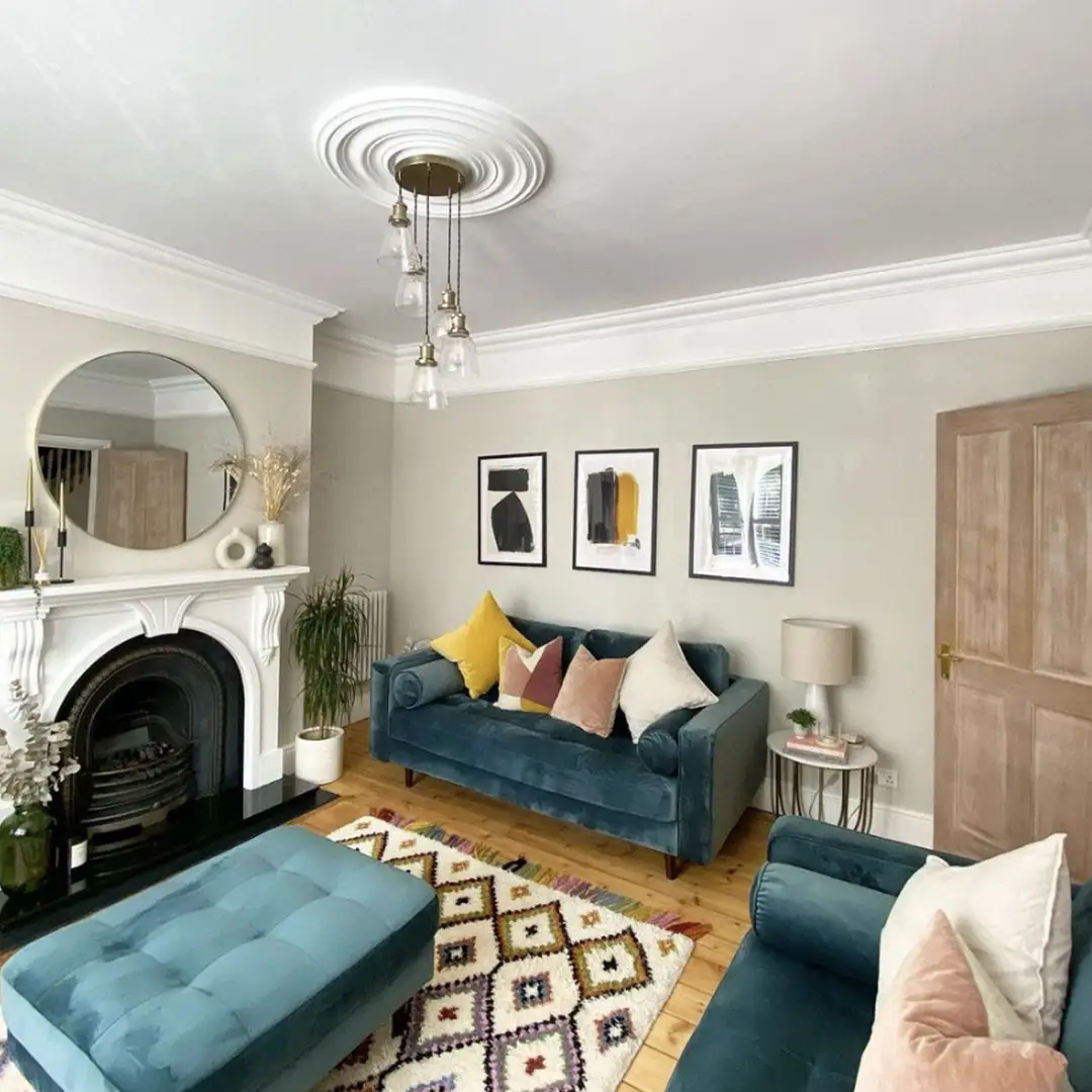 Colorful living room with teal-blue sofas, blue ottoman, mustard and blush cushions, patterned rug, and simple framed art.