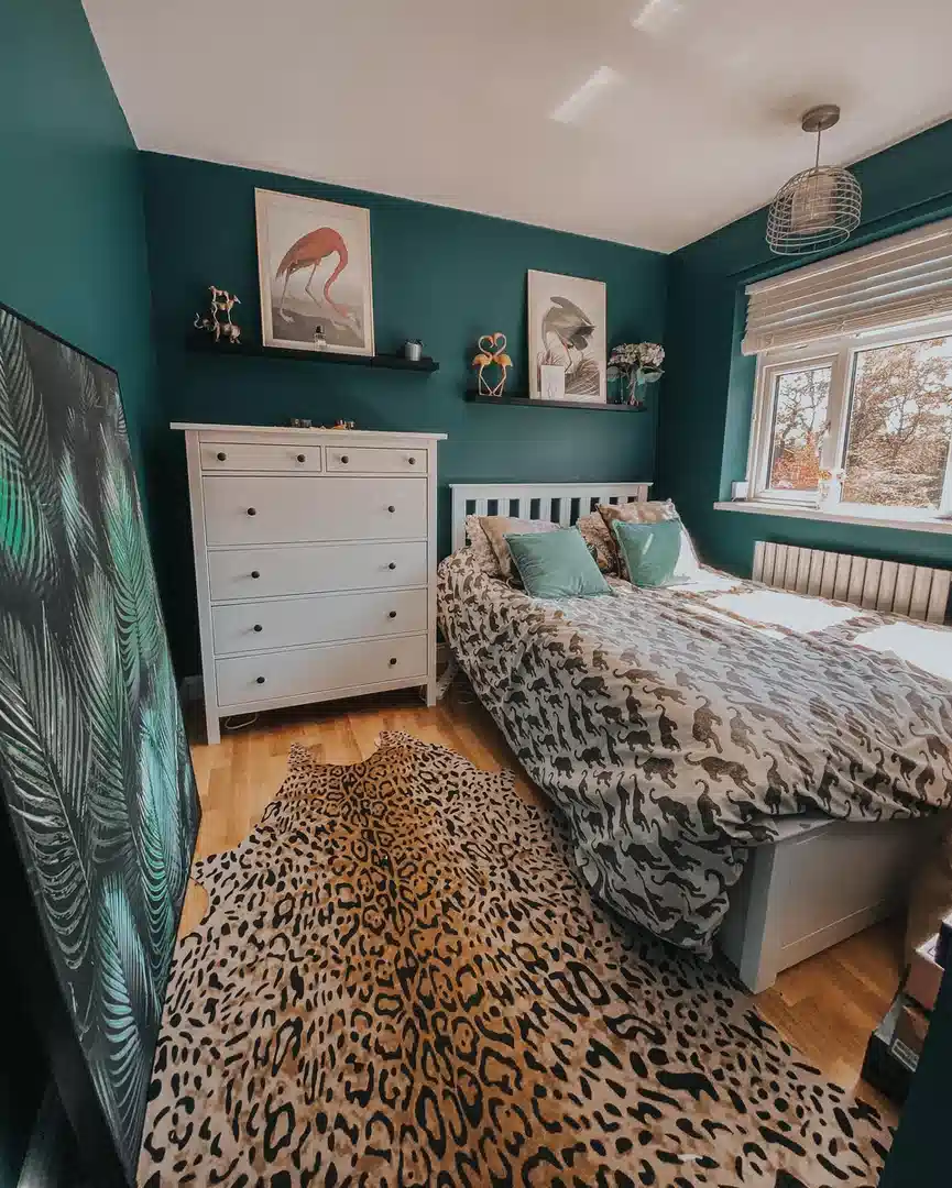 Leopard print rug in a bedroom with deep teal walls, white furniture and botanical artwork
