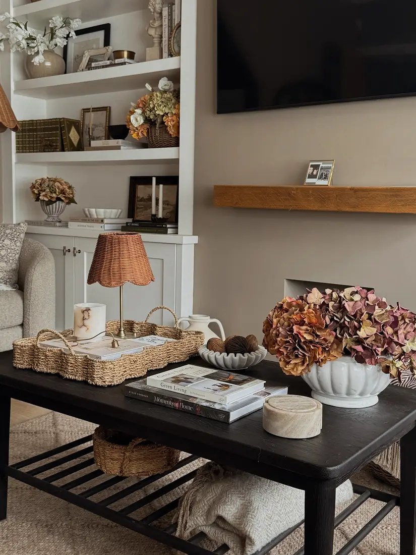 Chunky woven coffee table tray with small rattan lamp, candle, books, and white ceramic pitcher