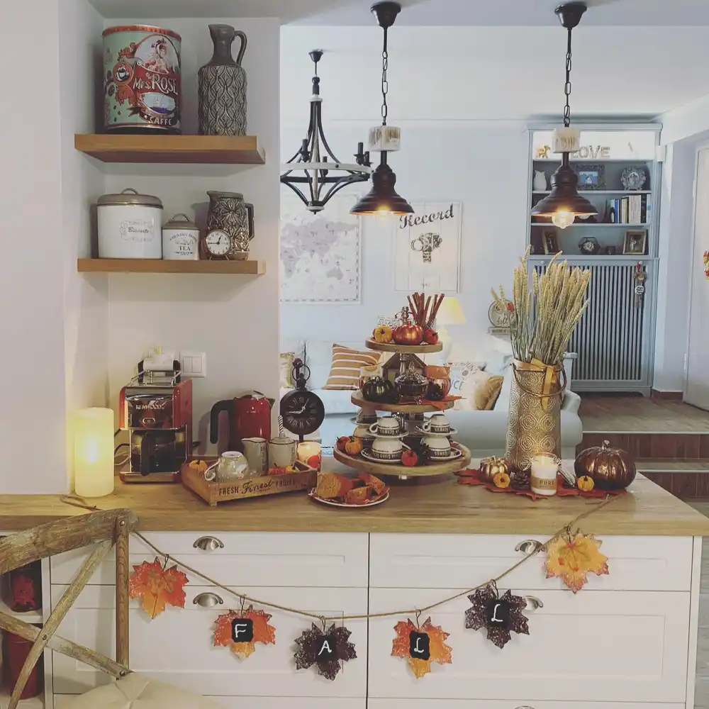 Fall coffee station with tiered tray, seasonal mugs, pumpkins, wheat stems, and coffee accessories on a kitchen island