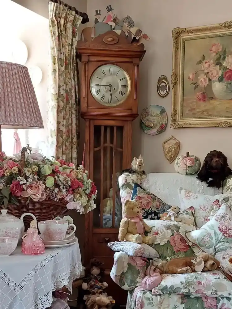 Vintage living room with tall grandfather clock, floral sofa, tea table, framed art, and china display
