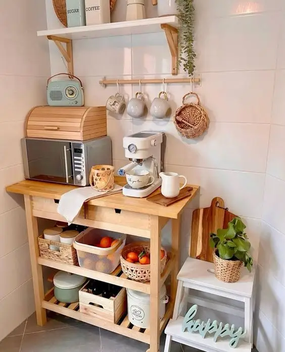 Small kitchen coffee station on wooden cart with espresso machine, hanging mugs, open storage baskets, and wall shelf