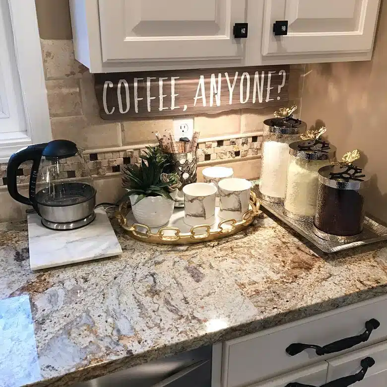 Small farmhouse coffee station on a kitchen counter with kettle, canisters, mugs on a gold tray, plant, and large wall sign