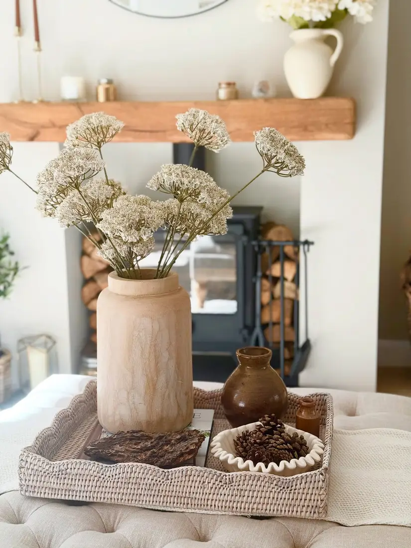 Neutral woven coffee table tray with pale wood vase, brown pottery, dried stems, and pinecones