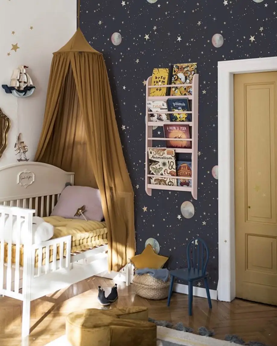 Space nursery with dark planet feature wall, white crib, light walls, and mustard canopy