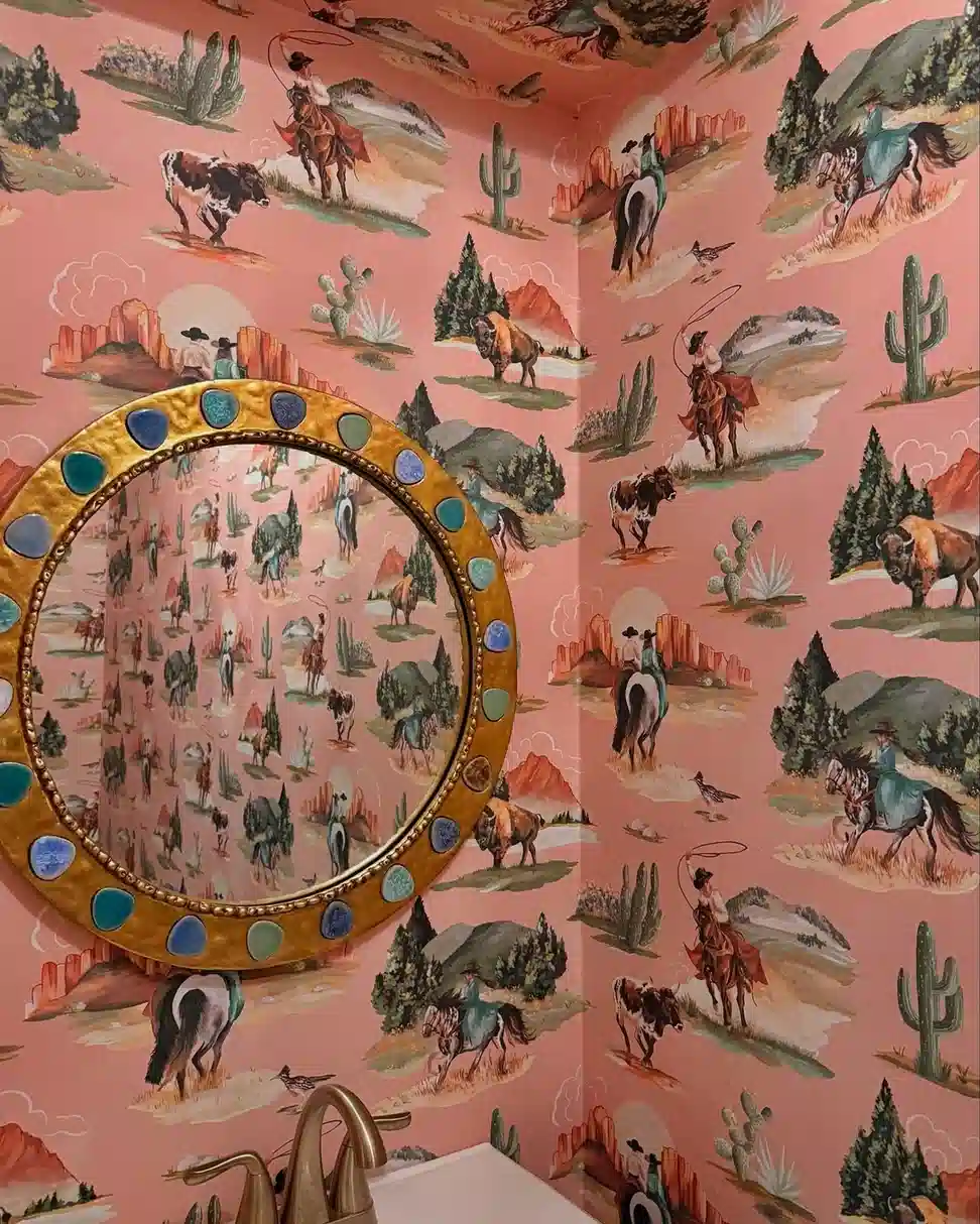 Pink western bathroom with cowboy wallpaper, gold jeweled mirror, white sink, and brass fixtures