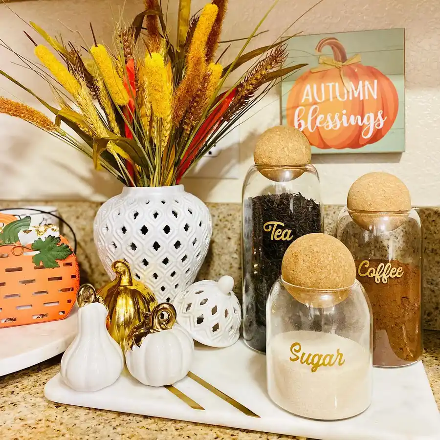 Fall coffee station with glass tea, coffee, and sugar canisters, white pumpkins, gold accents, and tall dried grasses