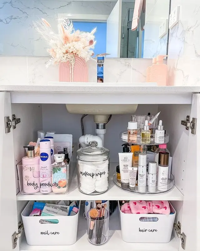 Bathroom sink cabinet with daily toiletries on the upper shelf and labeled bins for hair and nail products below