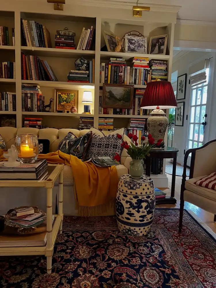 Cozy living room lined with full bookshelves, framed photos, small lamps, artwork, and comfortable seating.