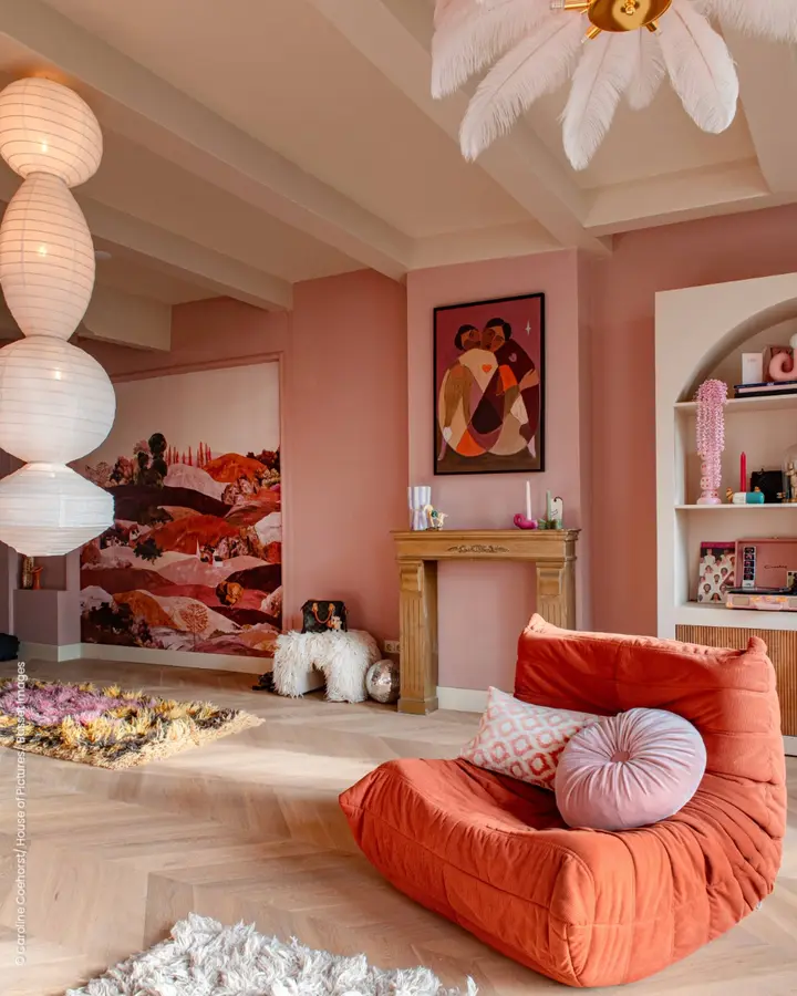 Tonal pink living room with dusty rose walls, coral lounge chair, pale cushions, warm artwork, and light wood flooring