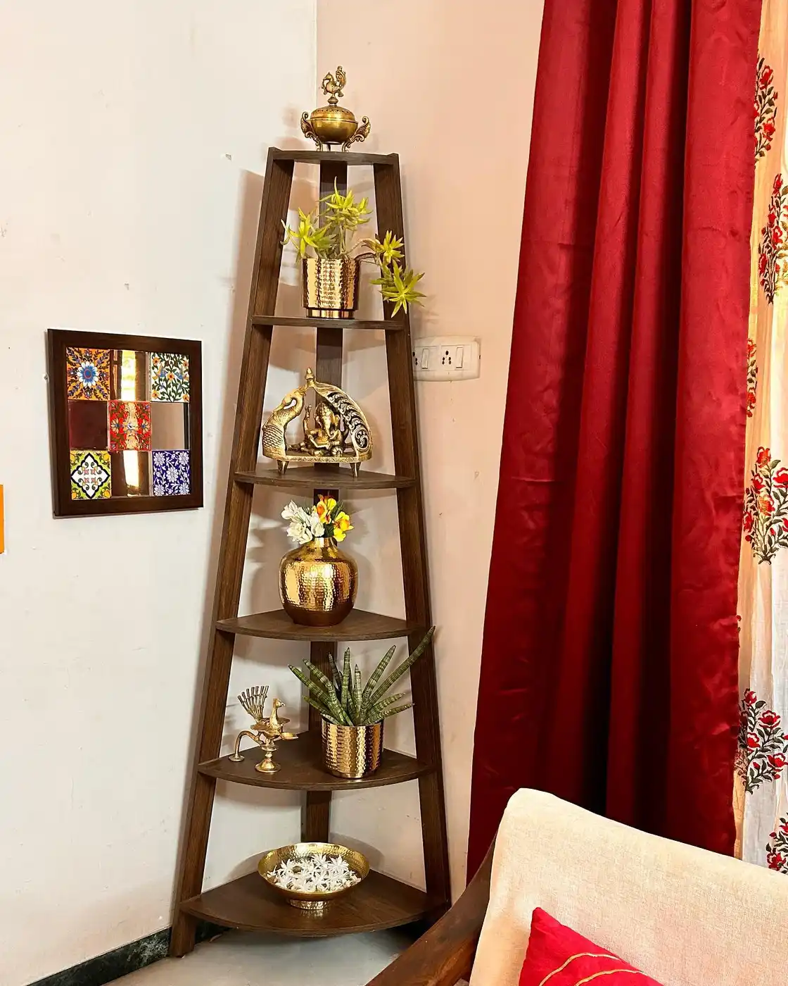 Tall wooden corner ladder shelf styled with brass decor, plants, flowers, and red curtains