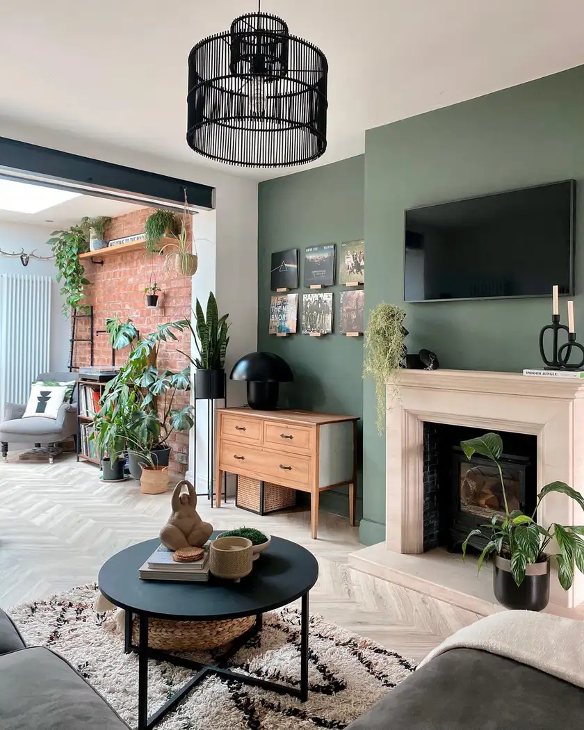 Character-filled living room with muted green walls, traditional fireplace, exposed brick, herringbone floor, and black lighting.