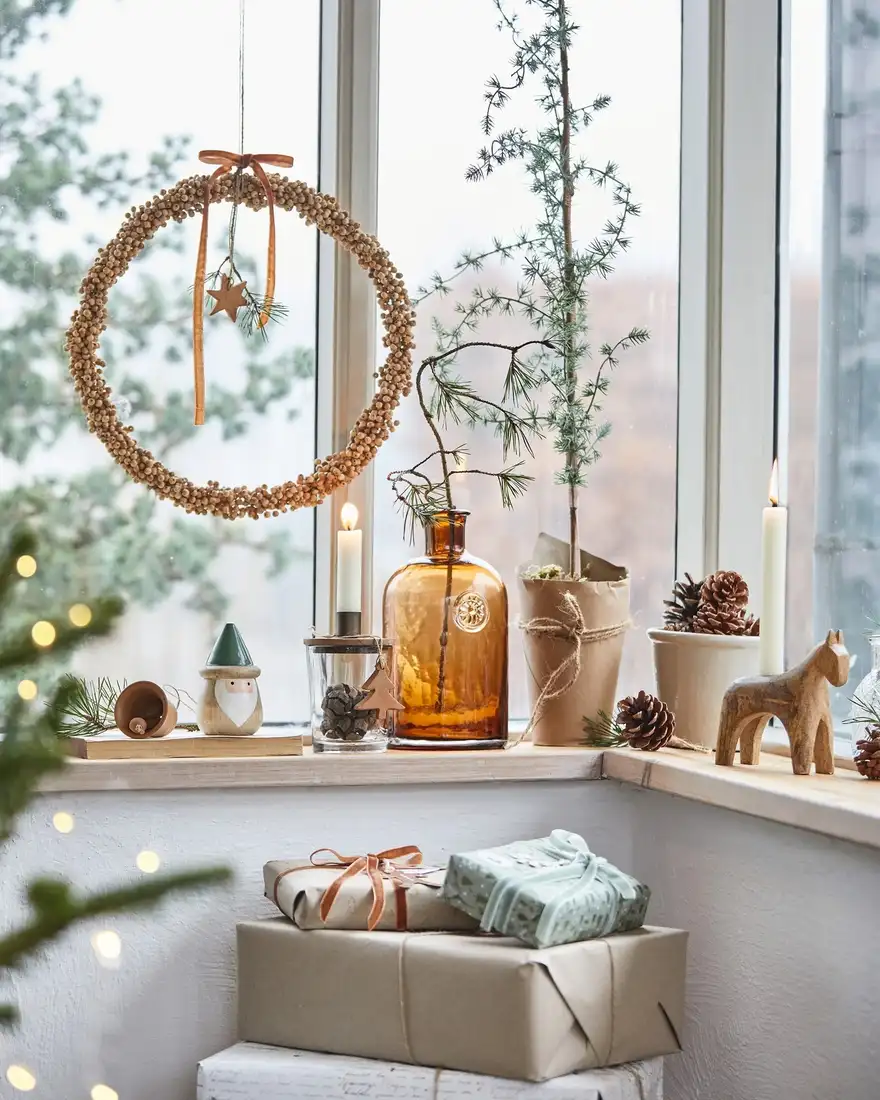 Winter kitchen window sill with wreath, candles, pinecones, small evergreen, and amber bottle