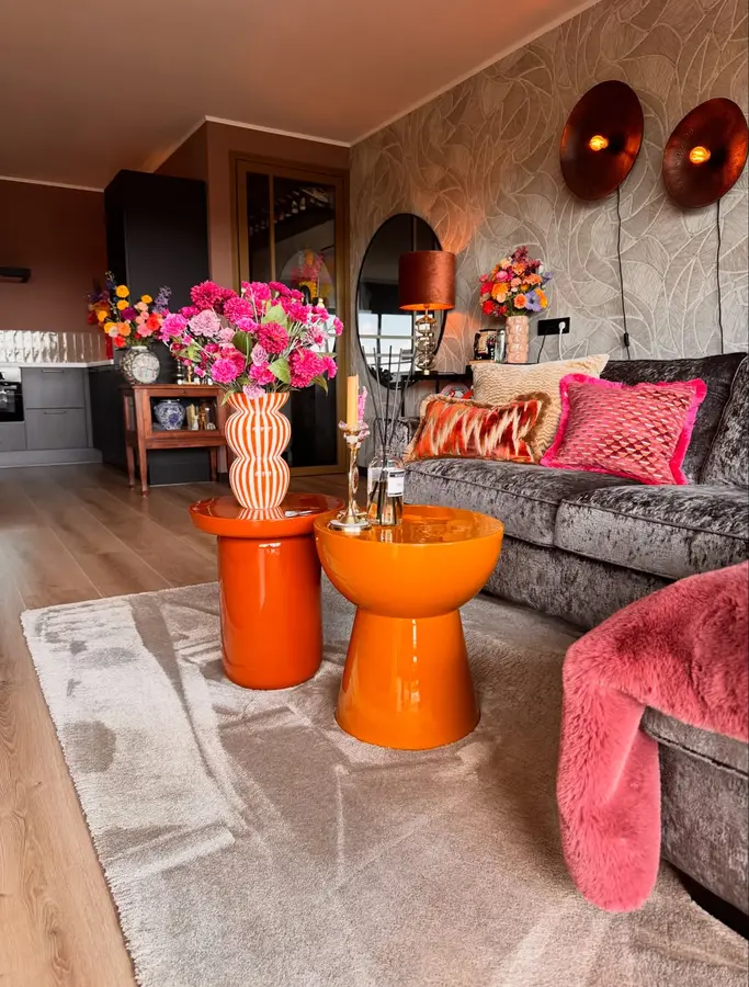 Gray living room brightened with glossy orange tables, hot pink cushions, colorful flowers, and neutral patterned rug