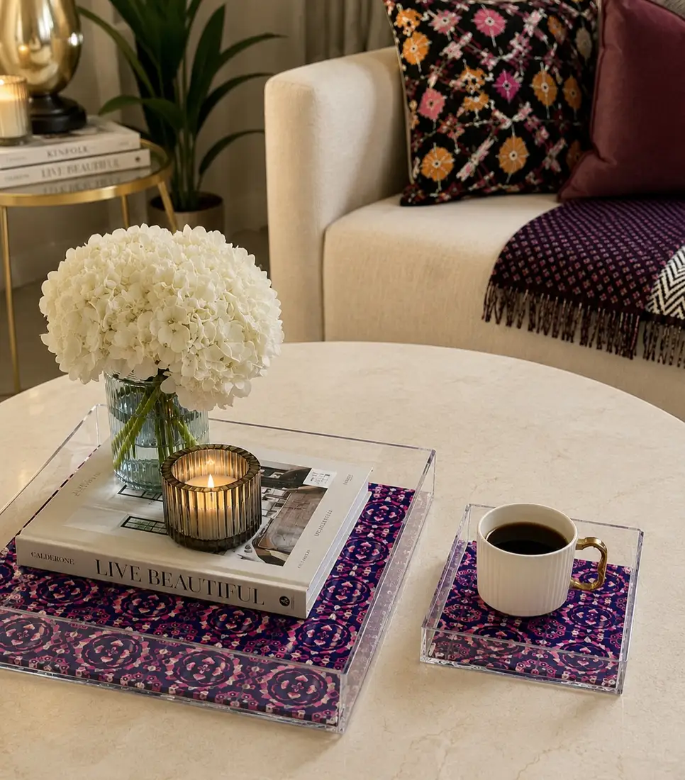 Clear acrylic coffee table trays with purple patterned liners, flowers, candle, book, and coffee cup