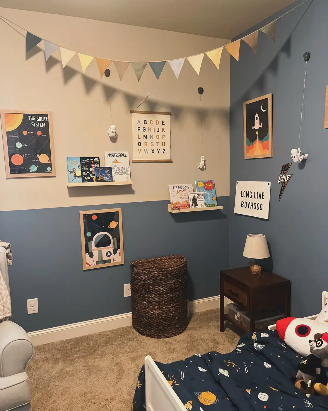 Kids bedroom with space prints, book ledges, hanging astronaut decor, bunting, and blue lower wall