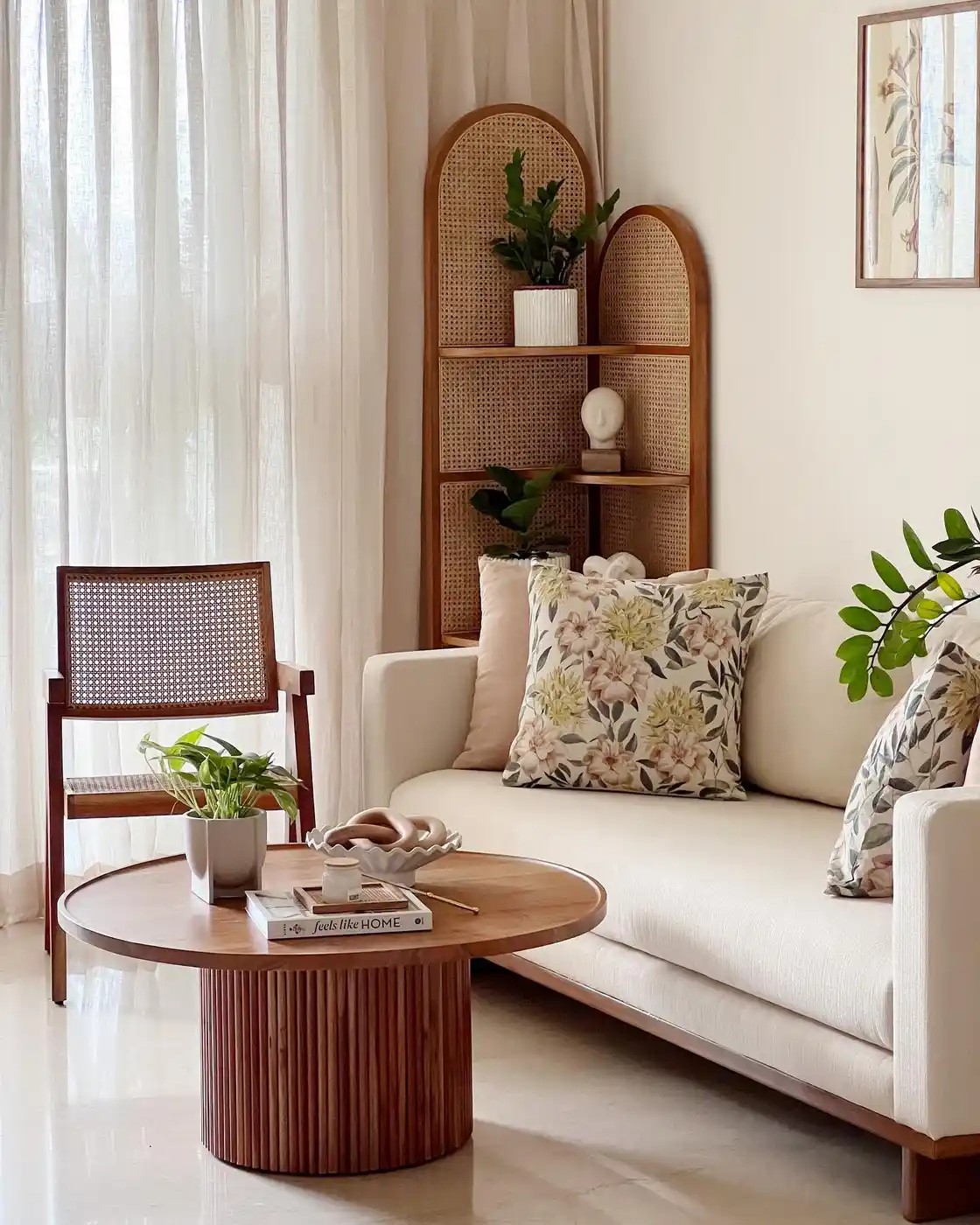 Bright living room corner with rattan shelving behind a cream sofa, cane chair, plants, and wood coffee table