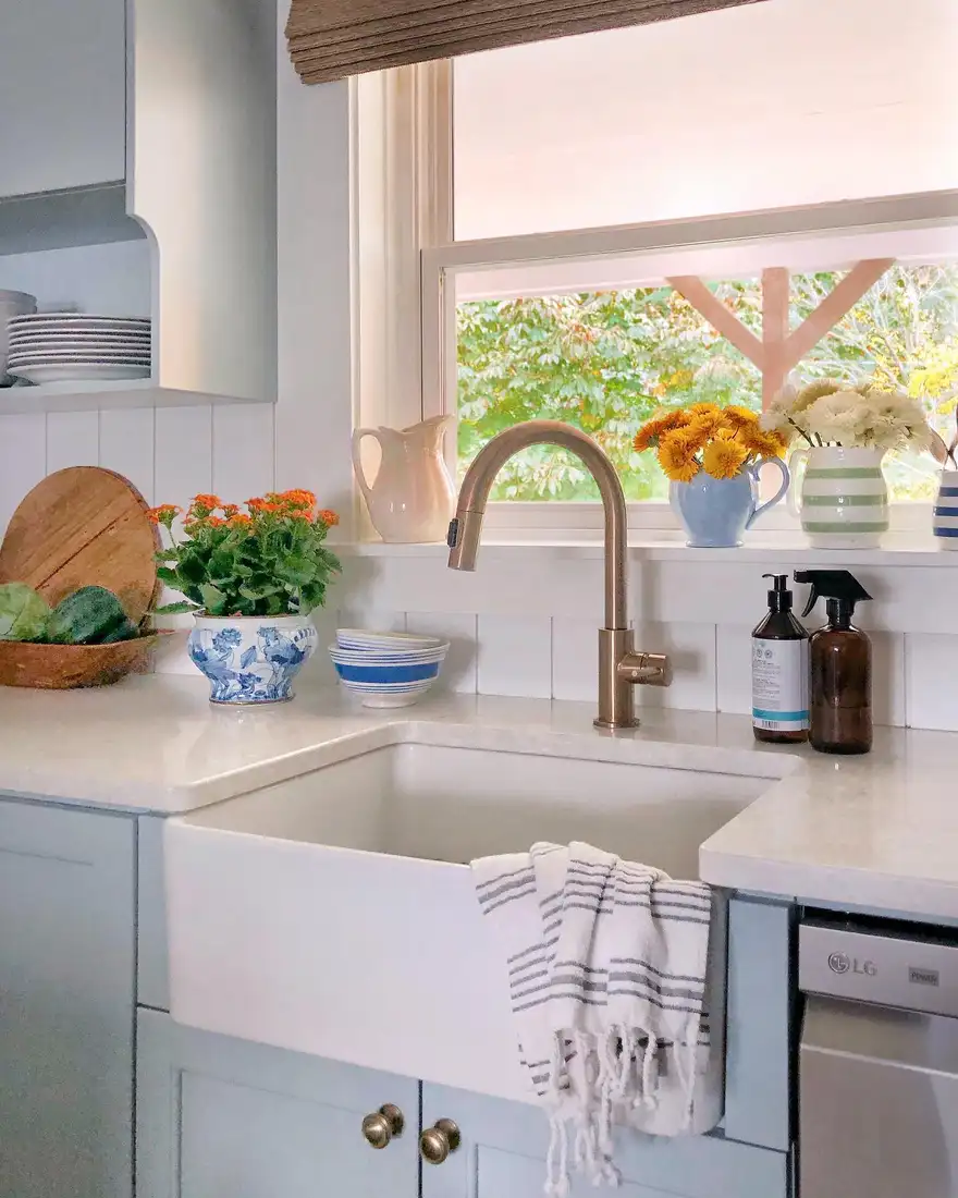 Kitchen window sill with colorful pitchers used as vases for orange and white flowers