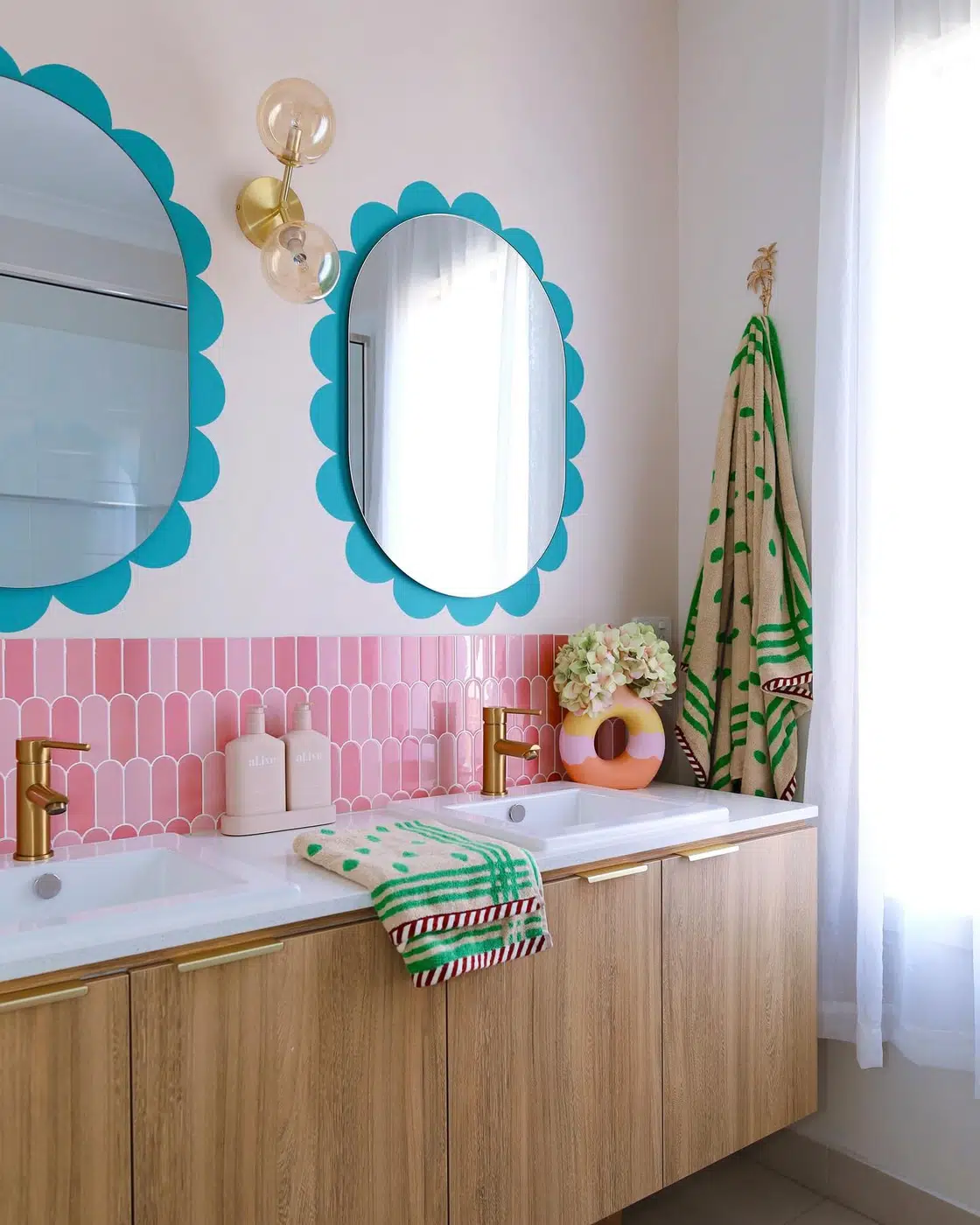 Bathroom vanity with turquoise scalloped mirrors, pink tile, wood cabinetry, and patterned towels