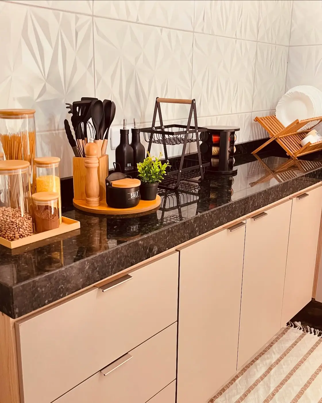 Long black kitchen counter organized into separate zones with glass canisters, cooking tools and dish rack