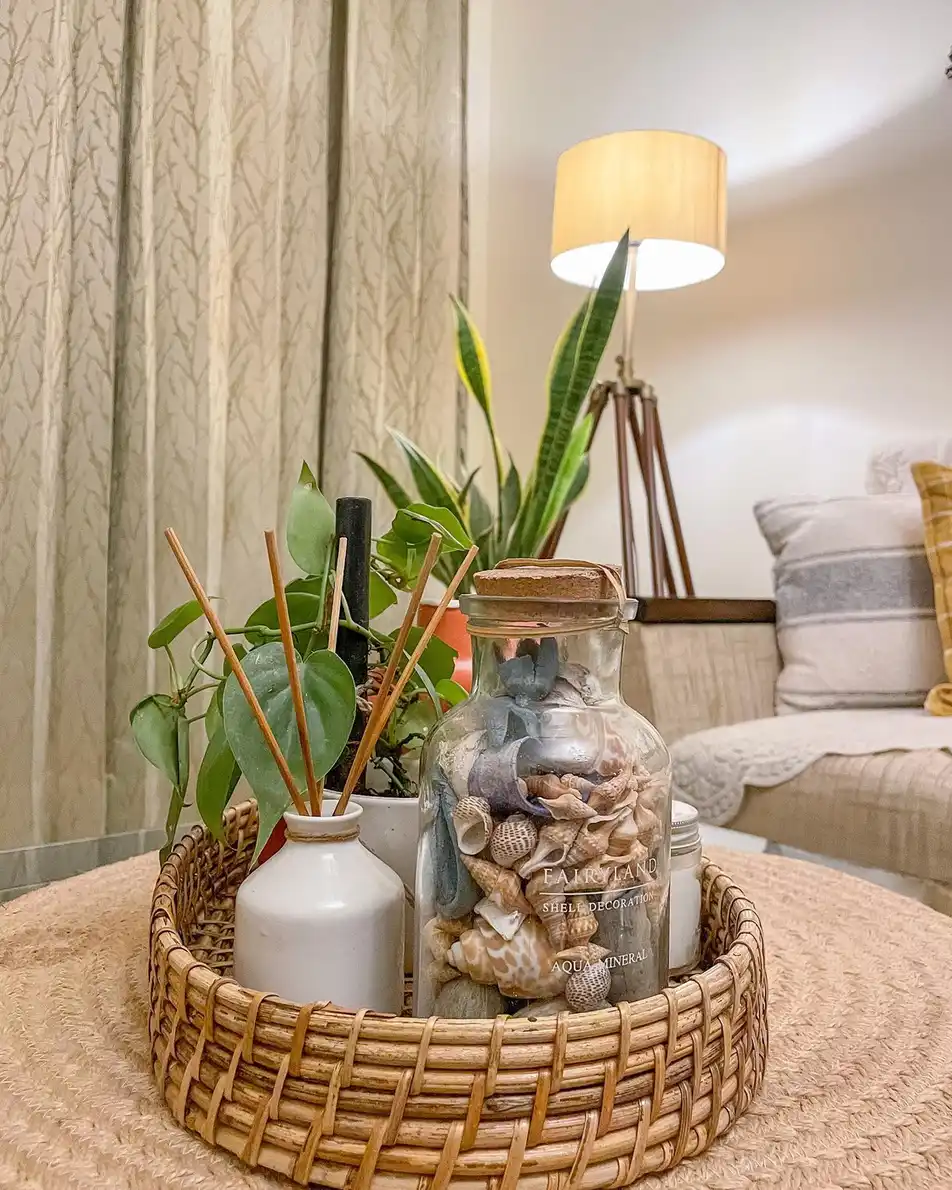 Neutral coffee table tray with wicker texture, glass jar of shells, leafy plant, and reed diffuser