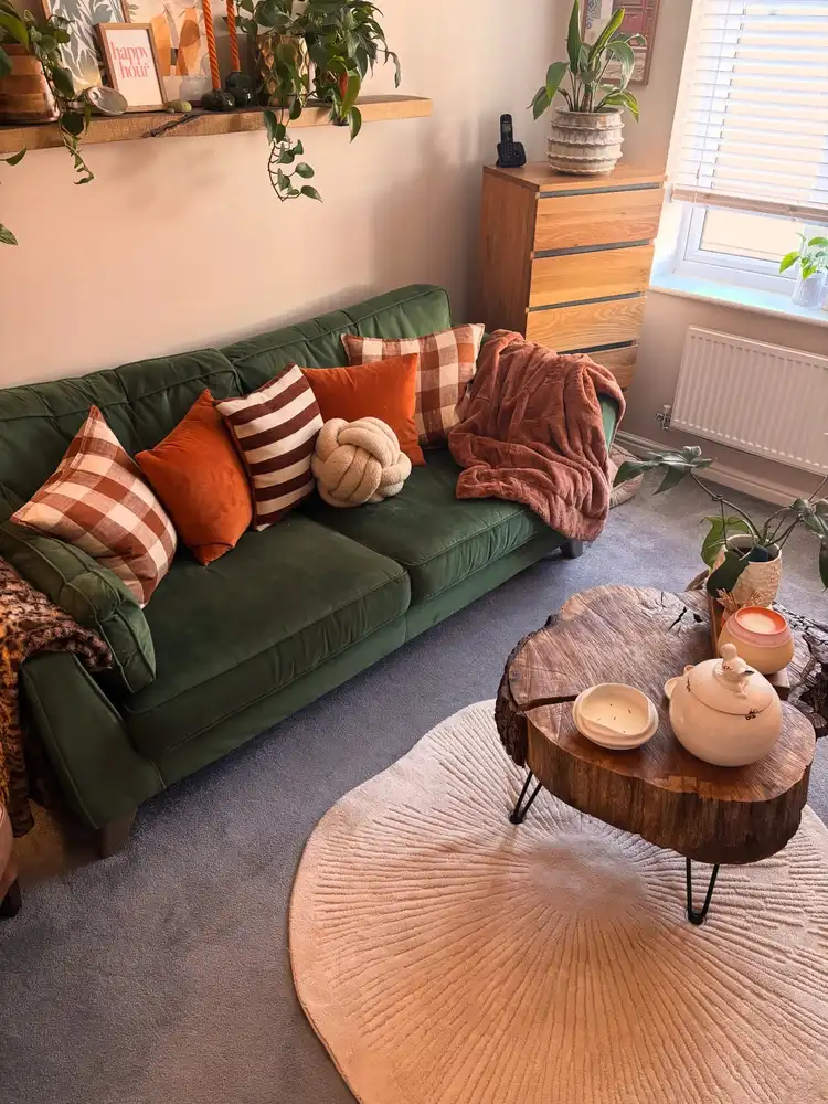 Dark green sofa styled with rust pillows, checked cushions, a warm throw, and a natural wood coffee table.