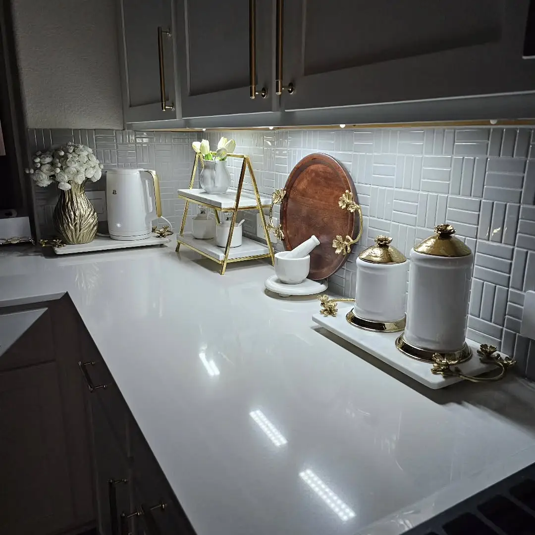 White kitchen counter with gold-accented canisters, tiered stand, flowers and large wooden serving board