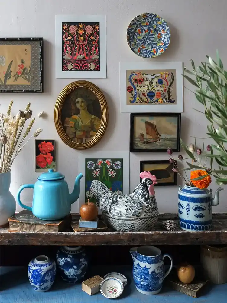 Collected vintage shelf with colorful pottery, blue and white ceramics, books, dried flowers, and small art