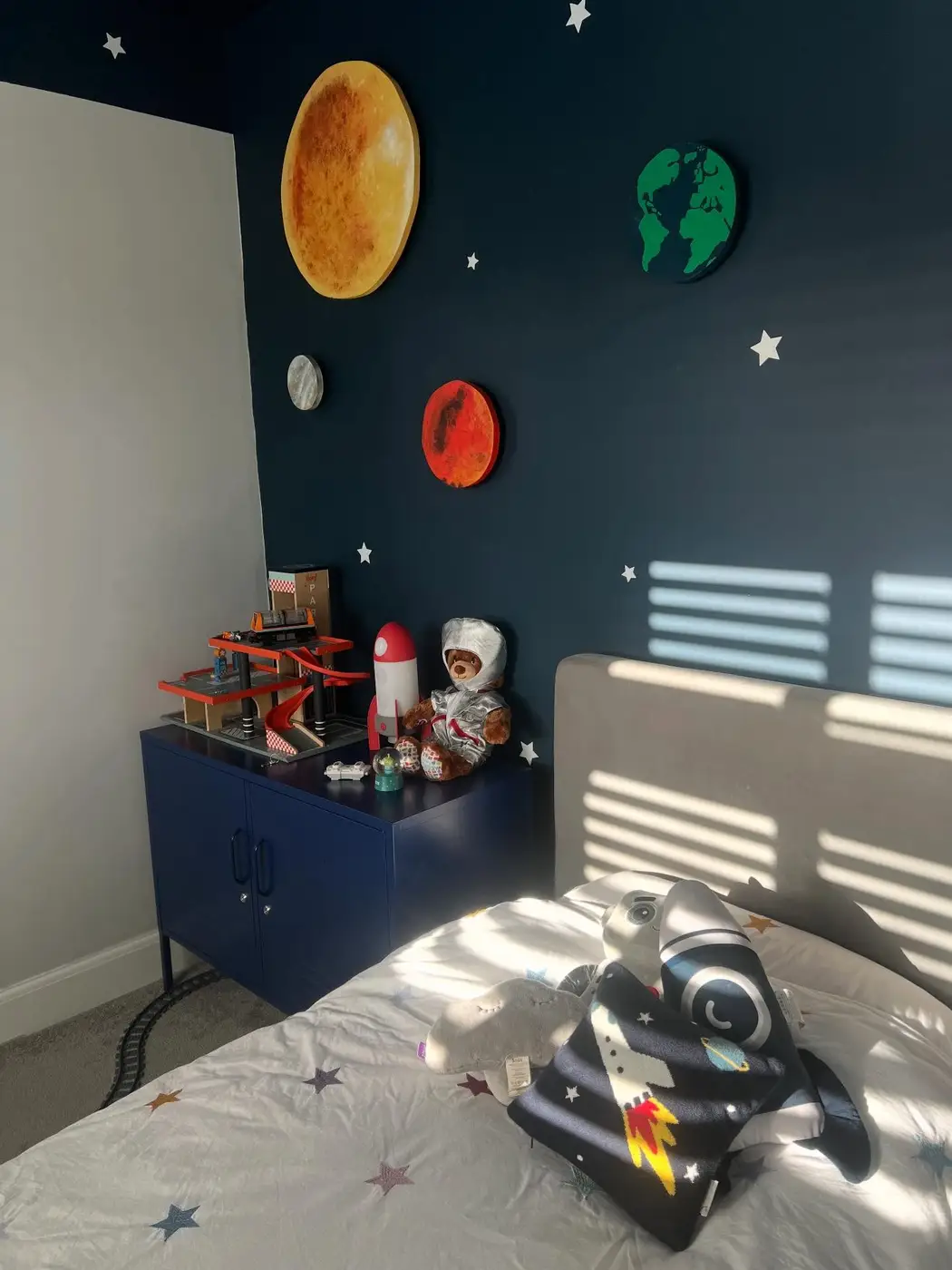 Kids space bedroom with large raised planet decorations on a dark wall and themed toys below