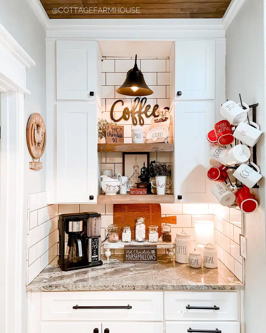 Built-in farmhouse coffee bar with white cabinets, subway tile, wood shelves, black pendant light, coffee machine, and seasonal red mugs