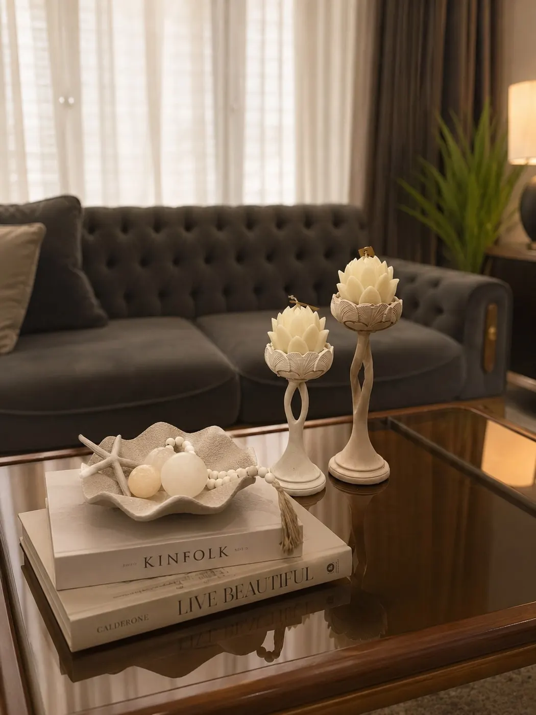 Glass coffee table with neutral books, cream candleholders, sculptural bowl, and decorative beads