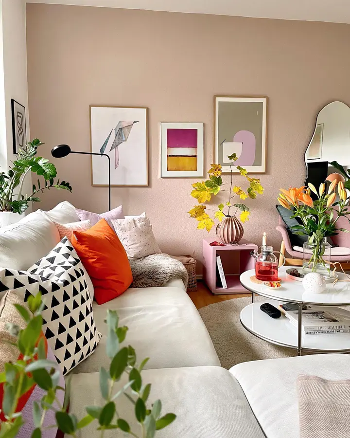 Soft colorful living room with blush walls, cream seating, orange cushion, black and white geometric pillow, flowers, and art