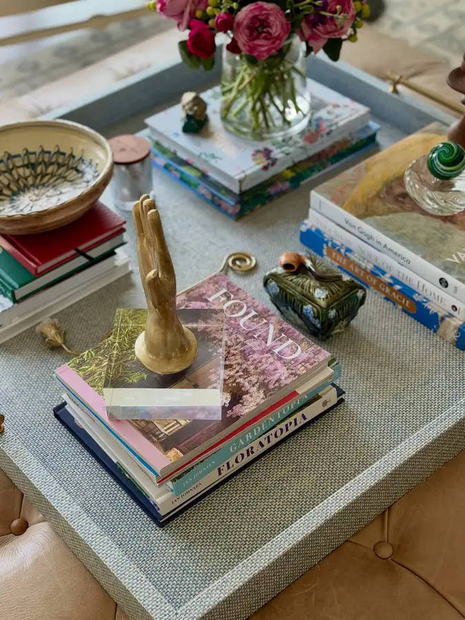 Large coffee table tray styled with stacked books, flowers, bowls, brass hand sculpture, and decorative objects