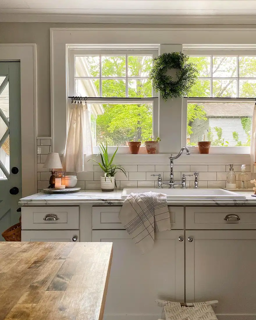 Kitchen sink window with a simple green wreath hanging between two windows and small pots below