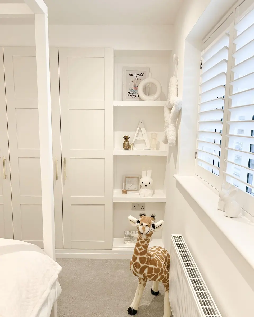 Small neutral bedroom with cream built-in wardrobes, open display shelves, white shutters, playful decor, and giraffe toy.