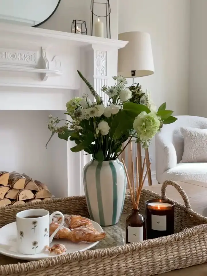 Woven coffee table tray with striped vase, white flowers, candle, reed diffuser, coffee mug, and pastries