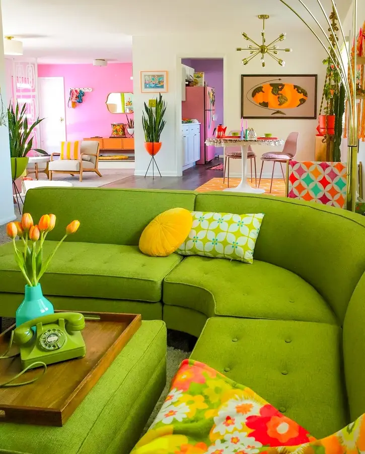 Bright living room with lime green sectional, yellow and orange cushions, colorful flowers, white walls, and vivid artwork