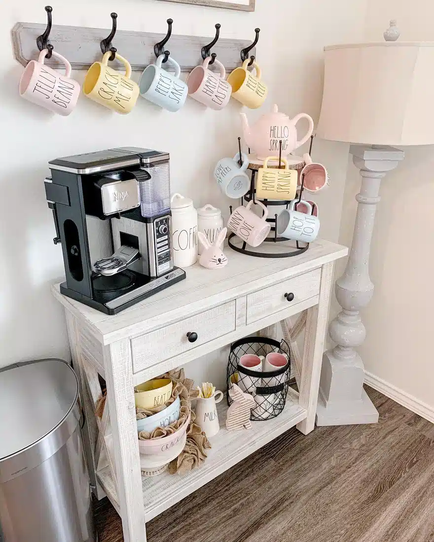 Spring farmhouse coffee bar with pastel mugs, whitewashed console, wall mug rack, round mug stand, pink teapot, and bunny decor