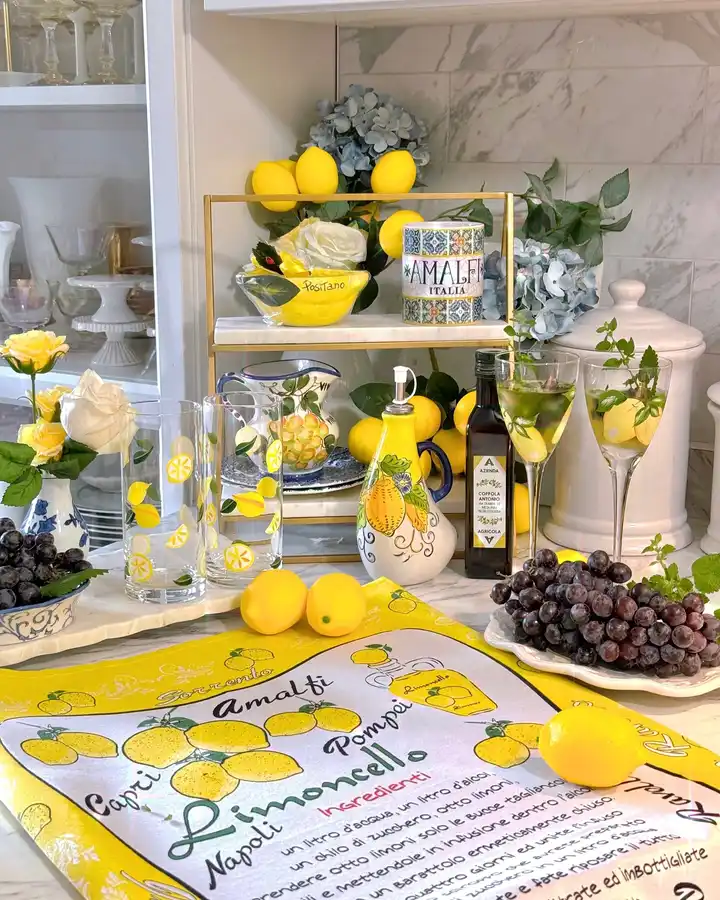 Bright lemon-themed kitchen counter with yellow fruit, decorative glassware, tiered stand, flowers and grapes