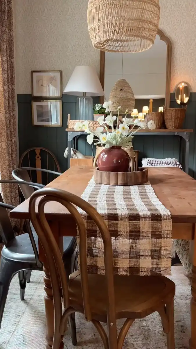Casual vintage dining room with worn wood table, woven pendant, checked runner, flowers, and large mirror