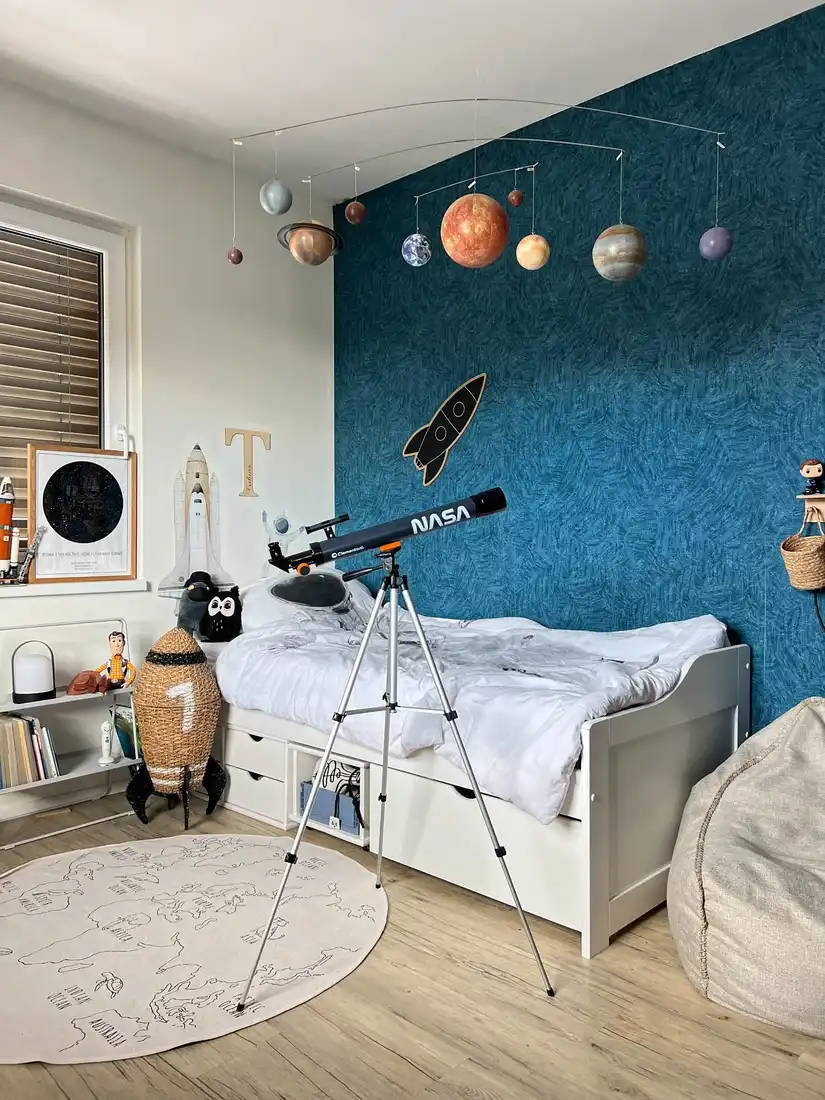 Space-themed kids bedroom with telescope, hanging planets, navy wall, and celestial decorations