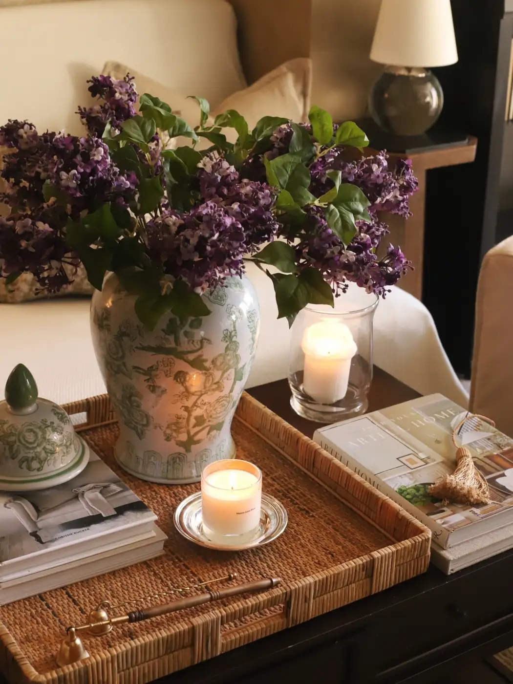 Coffee table with large rattan tray, purple flowers, patterned vase, books, candles, and decorative jar