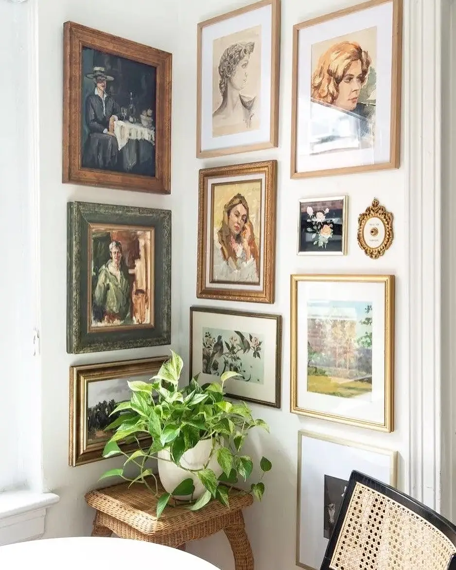 Gallery wall wrapping around a bright living room corner with mixed framed art, wicker stool, and leafy plant
